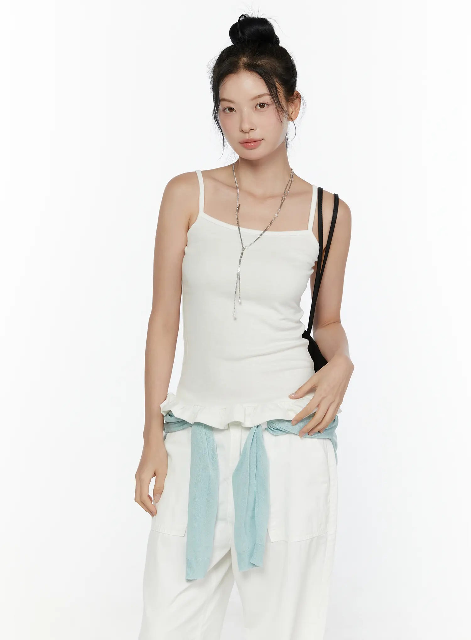 LEWKIN Ruffle Detail Cami Top CL521 White front shot on model with bun updo, spaghetti straps, ribbed knit body, ruffled hem, styled with white pants and light blue cardigan tied at waist