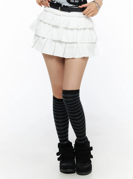 Ruffle Detail Mini Skirt IL523 White front close-up on model from waist down, standing pose with black belt, tiered pleats visible, styled with striped knee-high socks