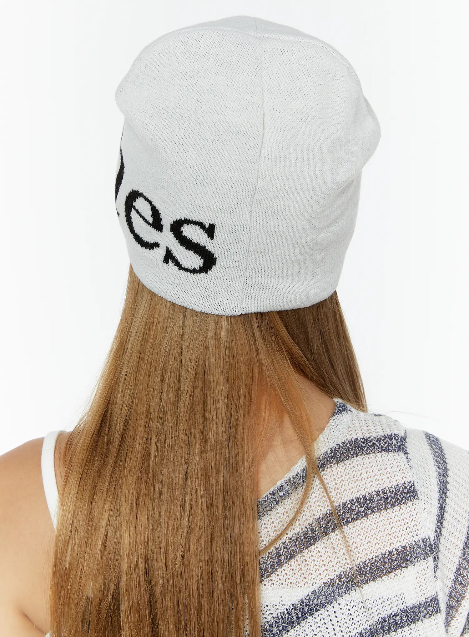 Sawyer Marches Beanie IL503 white back view on model showing black intarsia lettering on soft knit fabric, paired with striped top