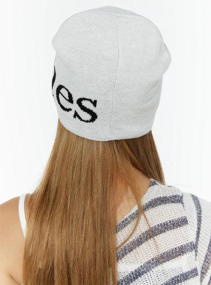Sawyer Marches Beanie IL503 white back view on model showing black intarsia lettering on soft knit fabric, paired with striped top