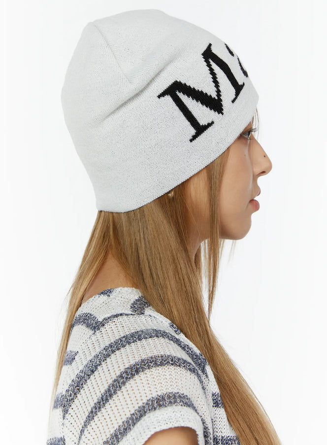 LEWKIN Sawyer Marches Beanie IL503 white side view on model with long hair wearing striped knit top, large black intarsia letter logo detail