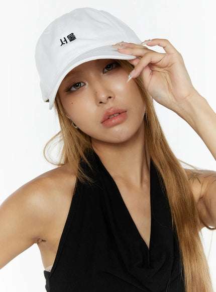 LEWKIN Seoul Mood Cap IL503 White close-up on model tilting brim with ringed hand, black halter top, soft cotton texture, Korean Hangul embroidery detail