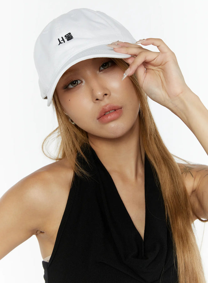LEWKIN Seoul Mood Cap IL503 White close-up on model tilting brim with ringed hand, black halter top, soft cotton texture, Korean Hangul embroidery detail