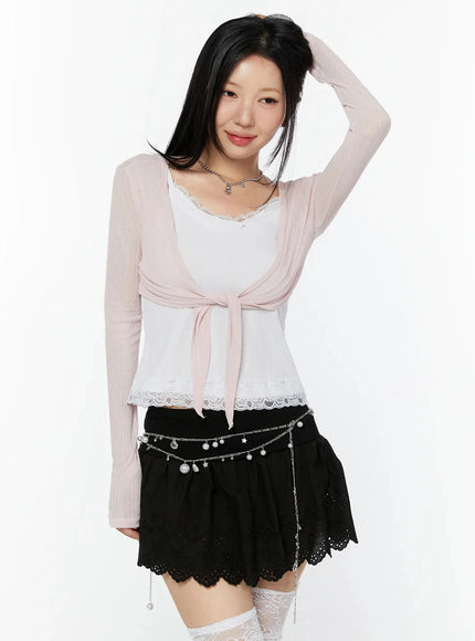 Sheer Front-Tie Wrap Cardigan IU524 Pink three-quarter front shot on model with hand touching ribbon tie detail over white lace-hem tank