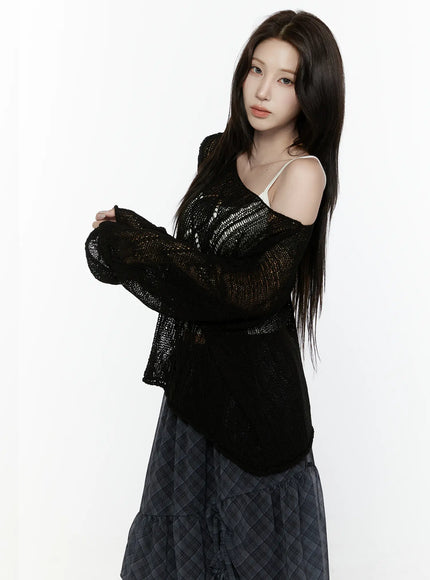 Sheer Knit Top IL522 Black side three-quarter shot on model with arms crossed showing sheer open-weave knit texture off-shoulder detail with white cami strap over dark plaid skirt