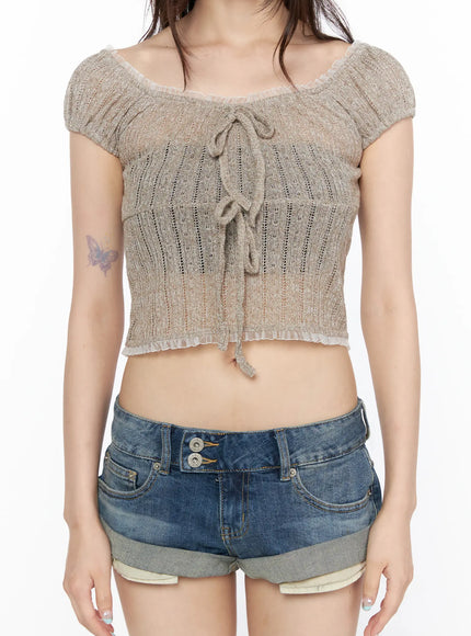 Sheer Lace Puff Sleeve Blouse CL523 Beige close-up front model shot showing lace-up tie, sheer ribbed knit fabric texture, frill hem detail, styled with denim shorts