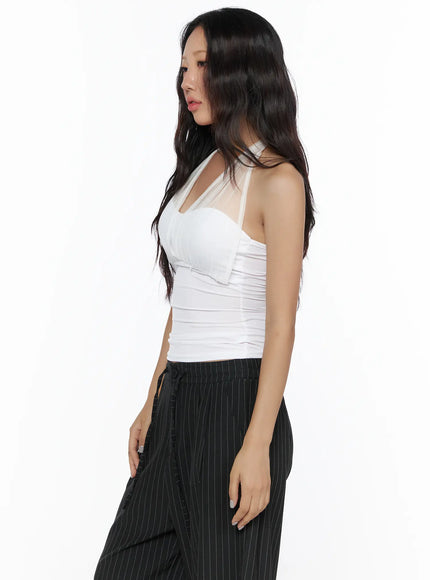 Sheer Layered Halter Top CL513 White three-quarter side model shot with baker boy cap, white top and navy pleated skirt over pinstripe trousers, hand on belt