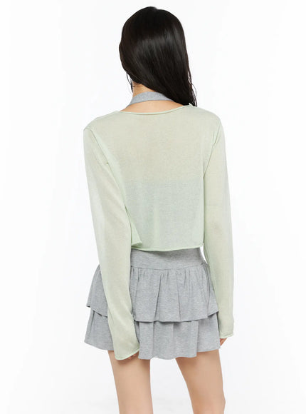 Sheer Lightweight Knit Cardigan CU530 Light green back view on model showing cropped hem and long sheer sleeves layered over gray sleeveless dress with tiered ruffles