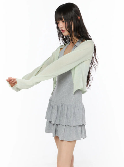 Sheer Lightweight Knit Cardigan CU530 Light green side view on model arms reaching forward showing sheer open-front crop length and full tiered gray ruffle skirt hem