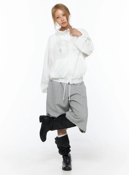 Sheer Nylon Windbreaker CU523 White front shot on model zipped up holding collar styled with gray drop-crotch pants and black knee-high boots