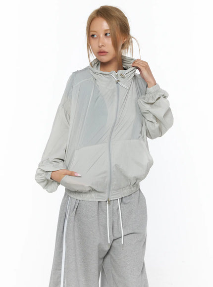 Sheer Nylon Windbreaker CU523 light gray front shot on model zipped up with hood adjusting hand wearing gray wide-leg pants lightweight nylon texture
