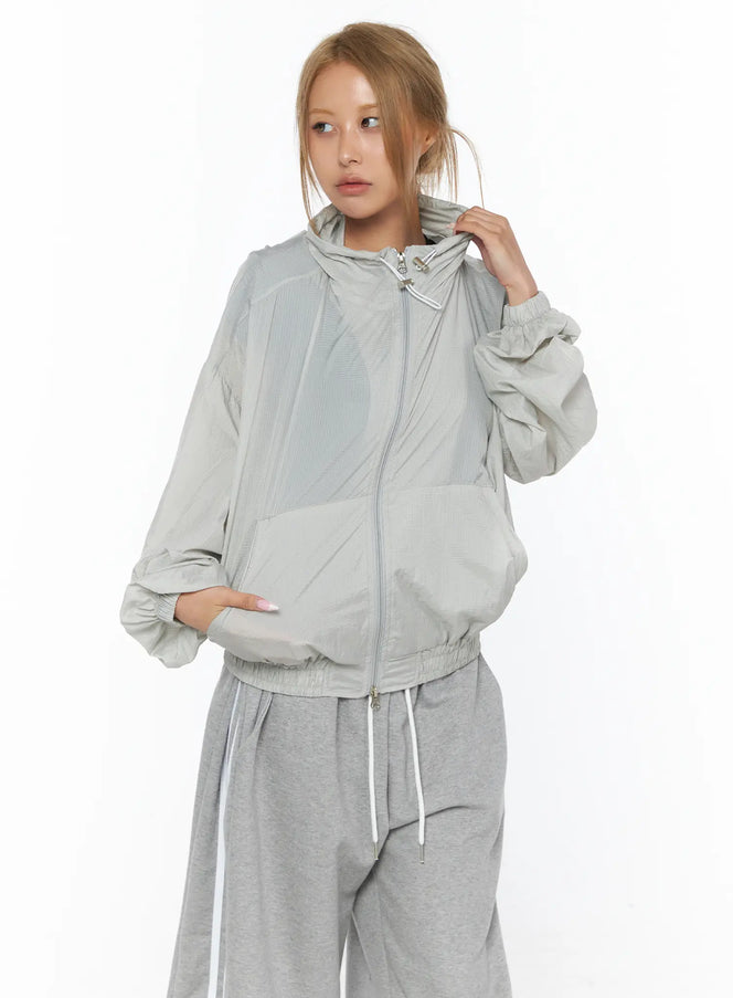 Sheer Nylon Windbreaker CU523 light gray front shot on model zipped up with hood adjusting hand wearing gray wide-leg pants lightweight nylon texture