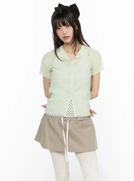 Sheer Pleated Short Sleeve Cardigan CL523 Light green front view on model arms at sides open over polka dot inner with beige drawstring skirt and white tights