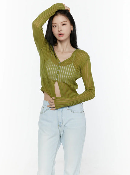 Sheer Ribbed Cardigan IL506 Green three-quarter front shot on model with hand raised to head unbuttoned showing sheer ribbed stripe knit cropped cardigan styled with light blue jeans