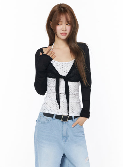 Sheer Tie-Front Wrap Crop Cardigan IL502 Black half-body front model shot model touching chest showing sheer wrap crop cardigan tie closure over polka dot tank top
