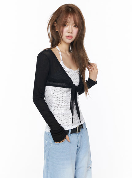 Sheer Tie-Front Wrap Crop Cardigan IL502 Black three-quarter angle model shot model touching hair showing sheer tie-front crop cardigan layered over polka dot cami
