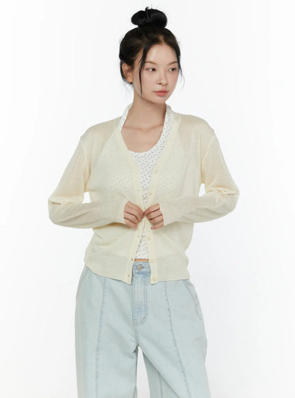 Sheer V-Neck Cardigan CL521 Light beige cropped front shot on model looking sideways hands at buttons showing V-neck and sheer lightweight knit texture