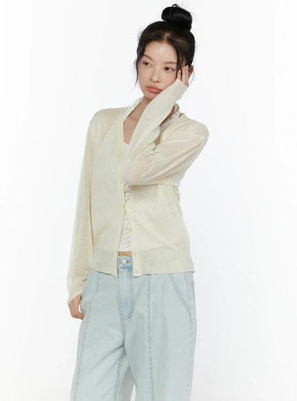 Sheer V-Neck Cardigan CL521 Light beige three-quarter front shot on model resting cheek on hand showing V-neckline sheer pointelle knit fabric and button placket