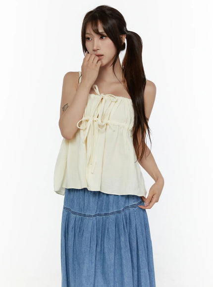 Shirred Cami Top CL508 Light beige three-quarter front shot on model with ponytail, smocked neckline and bow tie detail, flowy crinkle fabric, styled with blue denim skirt