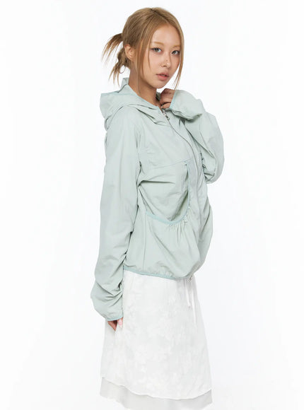 Shirred Hooded Windbreaker CU523 Mint side model hand on hood zip-up windbreaker showing side silhouette ruched waist pocket and elastic cuffs over white skirt