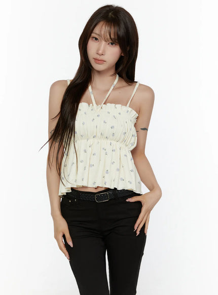 Shirred Ribbon Sleeveless Top CL507 Ivory front view on model in cream colorway with blue floral print, halter-style strap detail, paired with black pants and braided belt
