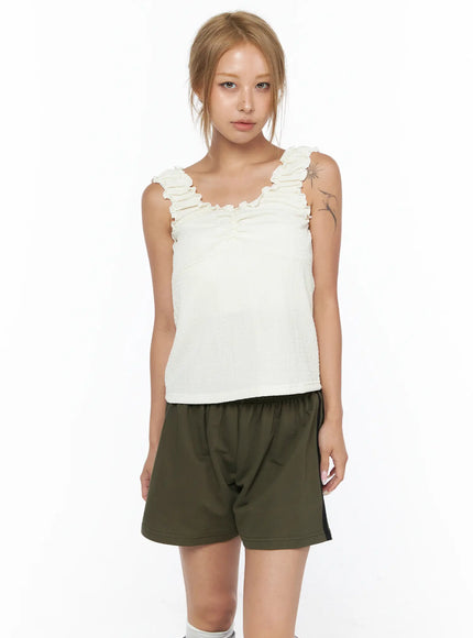 Shirred Ruffle Tank Top CU524 Light beige front view on model standing directly facing camera showing ruffle trim and smocked fabric with olive shorts
