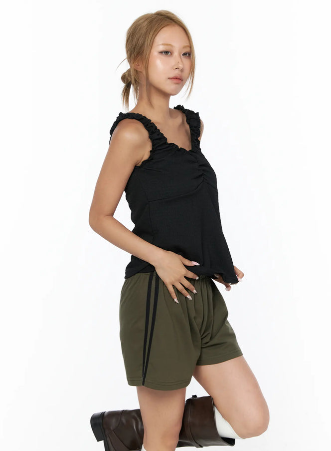 Shirred Ruffle Tank Top CU524 Black side view on model kneeling in olive shorts with black side stripe and dark brown boots