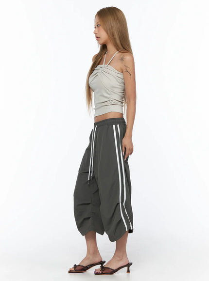 Shirred Strap Tube Top CU523 Light beige S/M side model shot showing asymmetric gathered fabric and crossover strap with gray wide-leg pants