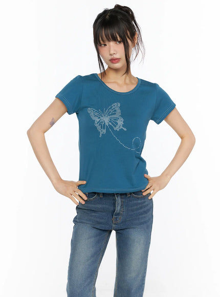 Short Sleeve Graphic Tee CU530 Blue front shot model hands-on-hips pose showing silver butterfly rhinestone graphic on teal cropped tee with blue jeans