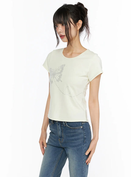 Short Sleeve Graphic Tee CU530 Light yellow three-quarter front shot model hands-on-waist pose showing butterfly rhinestone graphic and cropped hem with jeans