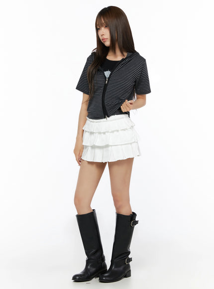 Short Sleeve Hooded Jacket IL523 Black three-quarter front view on model turning slightly, striped zip-up cropped hoodie with black knee-high boots and white ruffle mini skirt