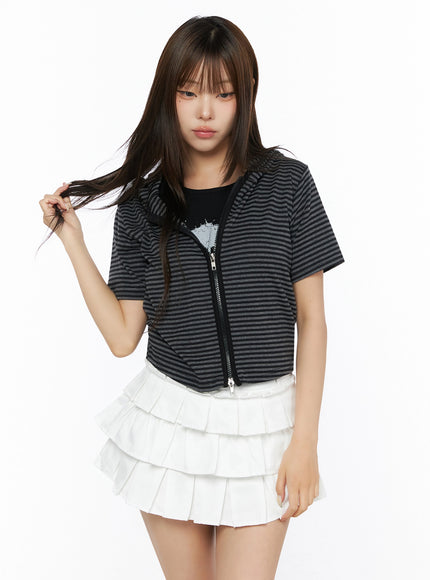 Short Sleeve Hooded Jacket IL523 Black front view on model with one hand in hair, striped short-sleeve zip-up hooded crop jacket, styled with white tiered pleated mini skirt