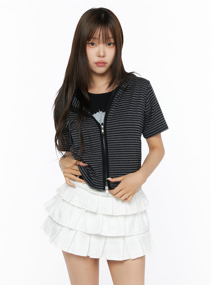 Short Sleeve Hooded Jacket IL523 Black front view on model hands at waist, zip-up striped cropped hooded jacket with short sleeves, paired with white layered ruffle mini skirt