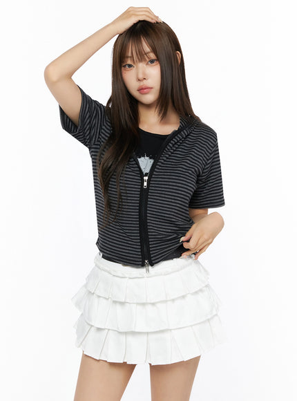 Short Sleeve Hooded Jacket IL523 Black front view on model with one hand raised to head, cropped striped zip-up hoodie with short sleeves, worn over white tiered pleated skirt