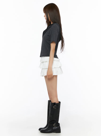 Short Sleeve Hooded Jacket IL523 Black side view on model showing cropped silhouette, horizontal stripe knit fabric, hood drape and short sleeve detail, styled with white ruffle skirt and boots
