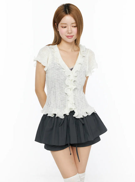 Short Sleeve Ruffle Cardigan CL501 White front model shot looking down with hand on hip, sheer ribbed knit ruffle cardigan styled with dark mini skirt