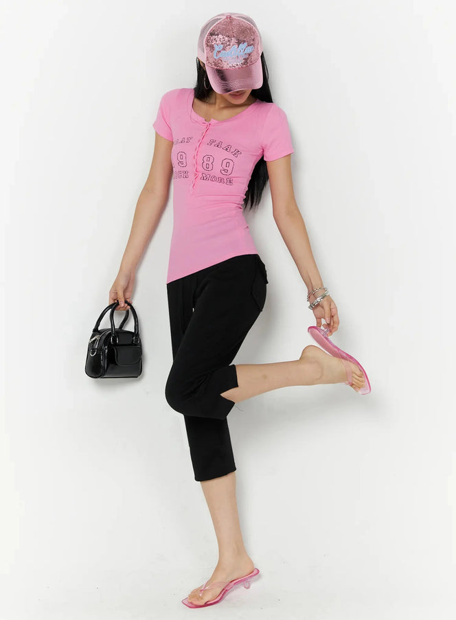 Side Slit Cropped Track Pants IL509 Black dynamic full-body styling shot on model wearing pink graphic tee, sequin cap, and pink sandals holding black bag one leg raised