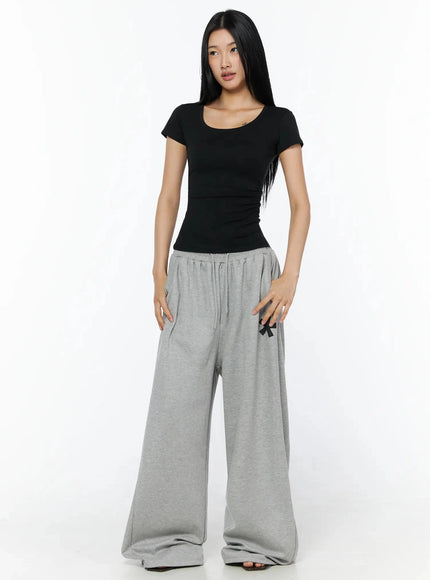 Silky Shirred Short Sleeve Tee IL509 Black front shot model standing upright scoop neckline fitted stretch fabric ruched waist paired with gray wide-leg drawstring sweatpants
