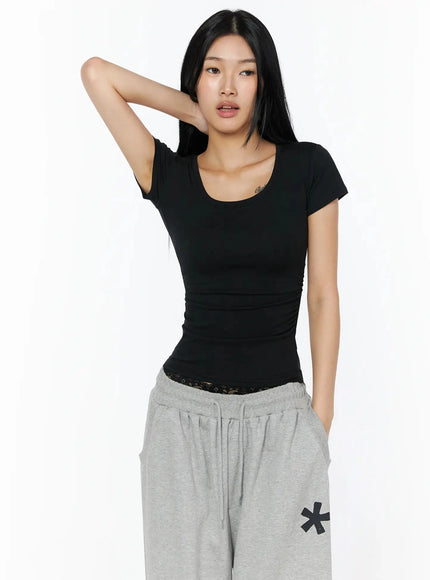 Silky Shirred Short Sleeve Tee IL509 Black three-quarter front shot model hand raised behind head relaxed pose showing fitted ruched silhouette styled with gray sweatpants