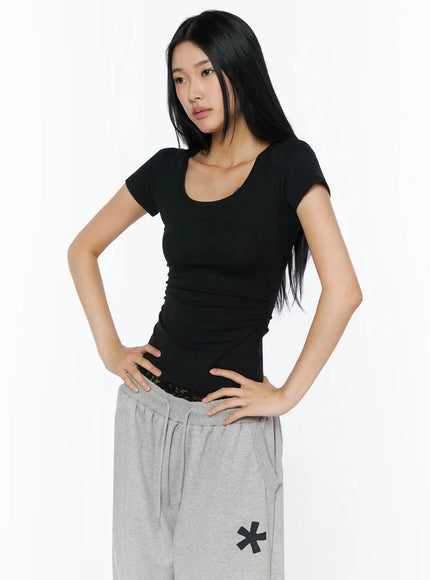 Silky Shirred Short Sleeve Tee IL509 Black front shot model hands on hips showing fitted ruched waist scoop neck short sleeve silhouette with lace waistband detail visible