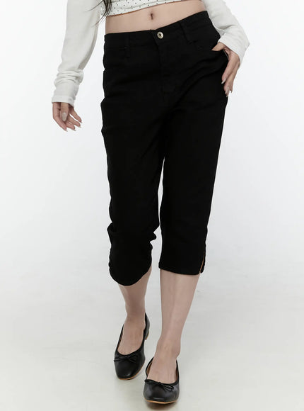 Slim Capri Pants IL521 Black front view on model walking pose showing drop-crotch fit, button fly, hand in pocket and slit hem