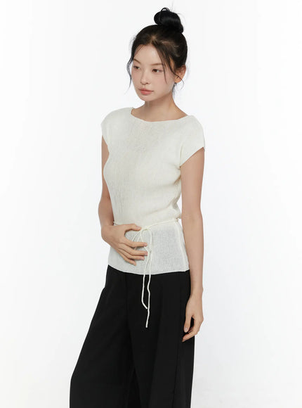 Slim Fit Boat Neck Knit Top CL520 Ivory three-quarter front shot on model with bun updo, ribbed knit cap sleeve top, boat neckline without choker string, side drawstring hem detail, black wide-leg pants