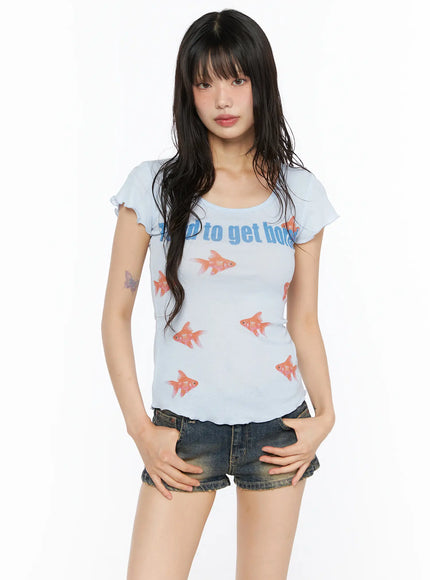 Slim Fit Graphic Tee CU530 Light Blue front shot on model with hands in pockets, featuring blue 'tend to get bored' text, allover red goldfish print, and lettuce-edge hem detail