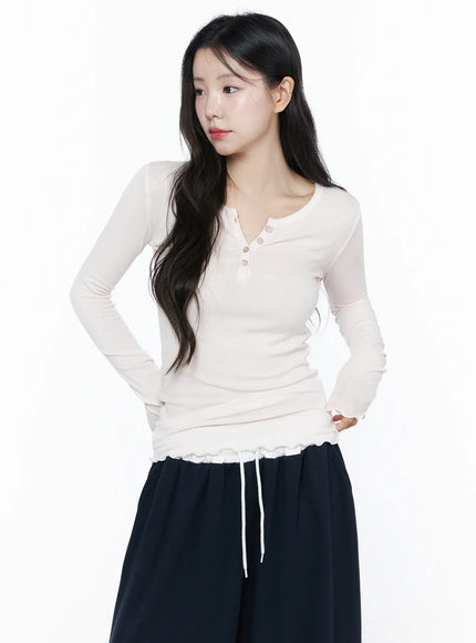 Slim-Fit Henly Neck Long Sleeve Tee IU525 Light pink front model shot hands on hips, henley buttons and ruffle hem visible, styled with dark trousers