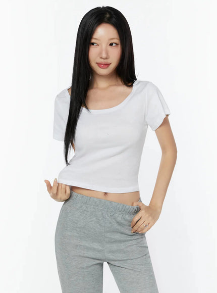 Slim U-Neck Short Sleeve Tee IU524 White cropped front shot on model with hand raised, paired with gray wide-leg sweatpants, ribbed cotton fabric