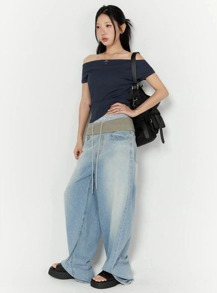 Solene Vintage Washed Foldover Baggy Jeans IU524 Blue three-quarter front shot on model carrying black bag hand on hip showing lace undergarment peeking above waistband