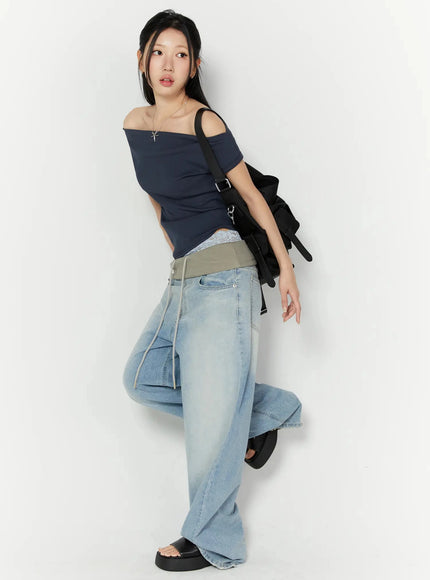 Solene Vintage Washed Foldover Baggy Jeans IU524 Blue three-quarter side shot on model in dynamic pose with raised knee styled with navy off-shoulder top and black bag