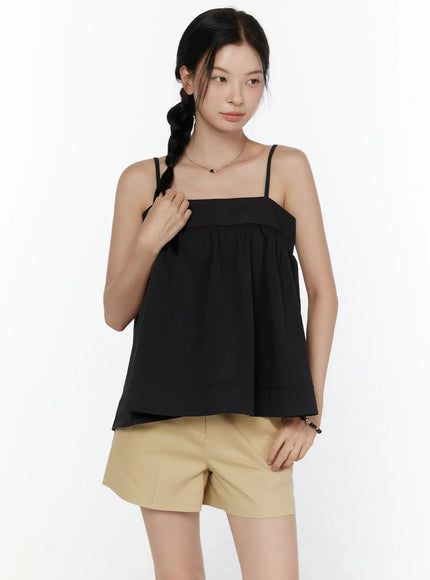 Square Neck Babydoll Cami Top CL520 Black front shot on model with hand raised to strap, styled with beige shorts, relaxed A-line silhouette