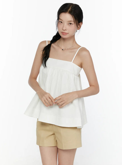 Square Neck Babydoll Cami Top CL520 White three-quarter front shot on model with hands clasped at waist, showing gathered empire waist and flowy cotton fabric
