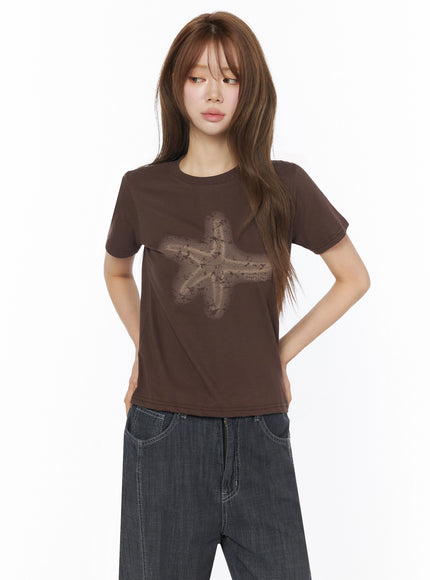 Star Graphic Tee IU525 Brown front model shot with faded star graphic print on fitted cotton tee styled with dark wide-leg jeans hands behind back